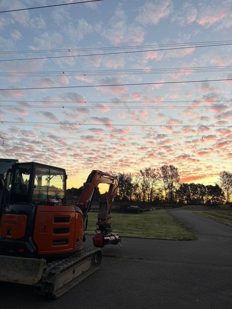 Sunset sky with colorful clouds behind an excavator on a gravel path.