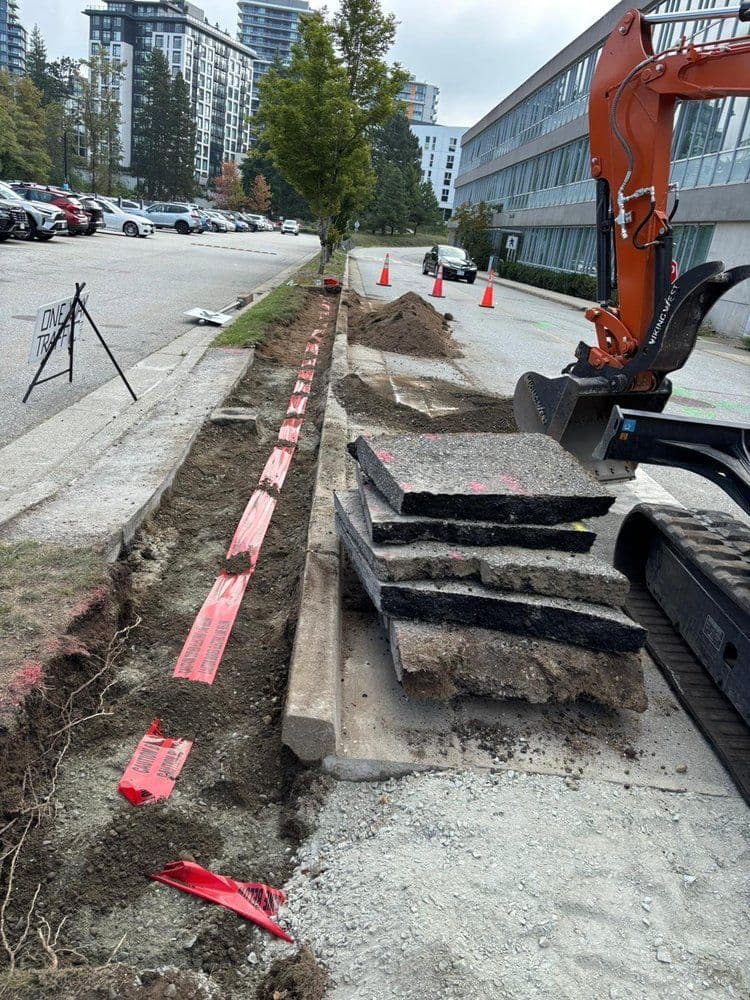 Construction site with an excavator, removed pavement, and safety cones lining the road.