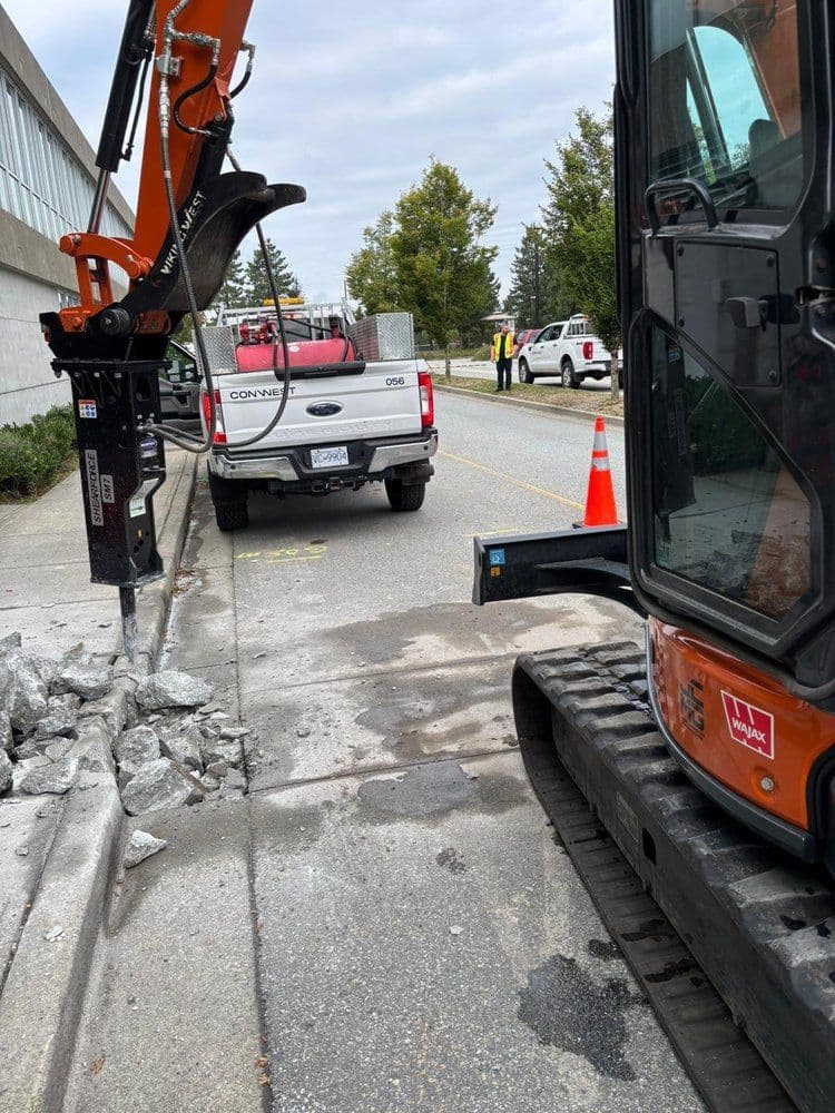 Heavy machinery digging near a truck on a road, with construction debris visible.