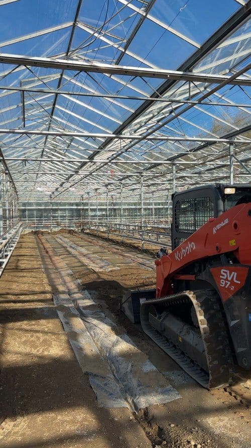 Kubota SVL95-2 compact track loader in a spacious greenhouse under a clear blue sky.