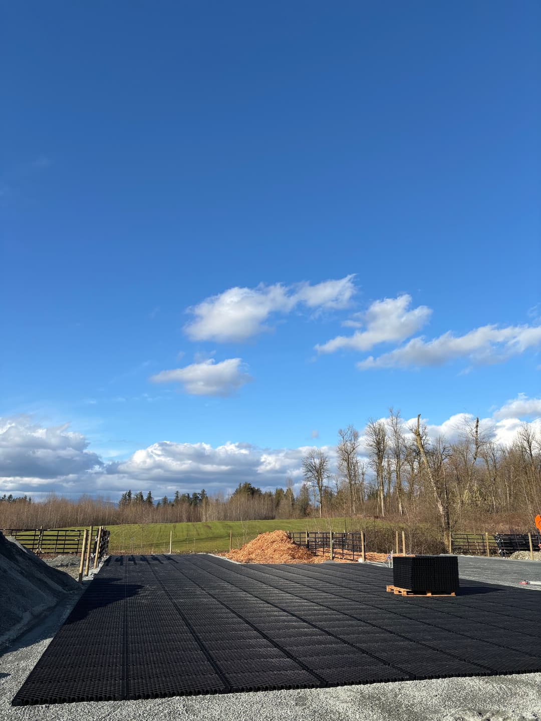 Construction site with black grid foundation under a clear blue sky and scattered clouds.