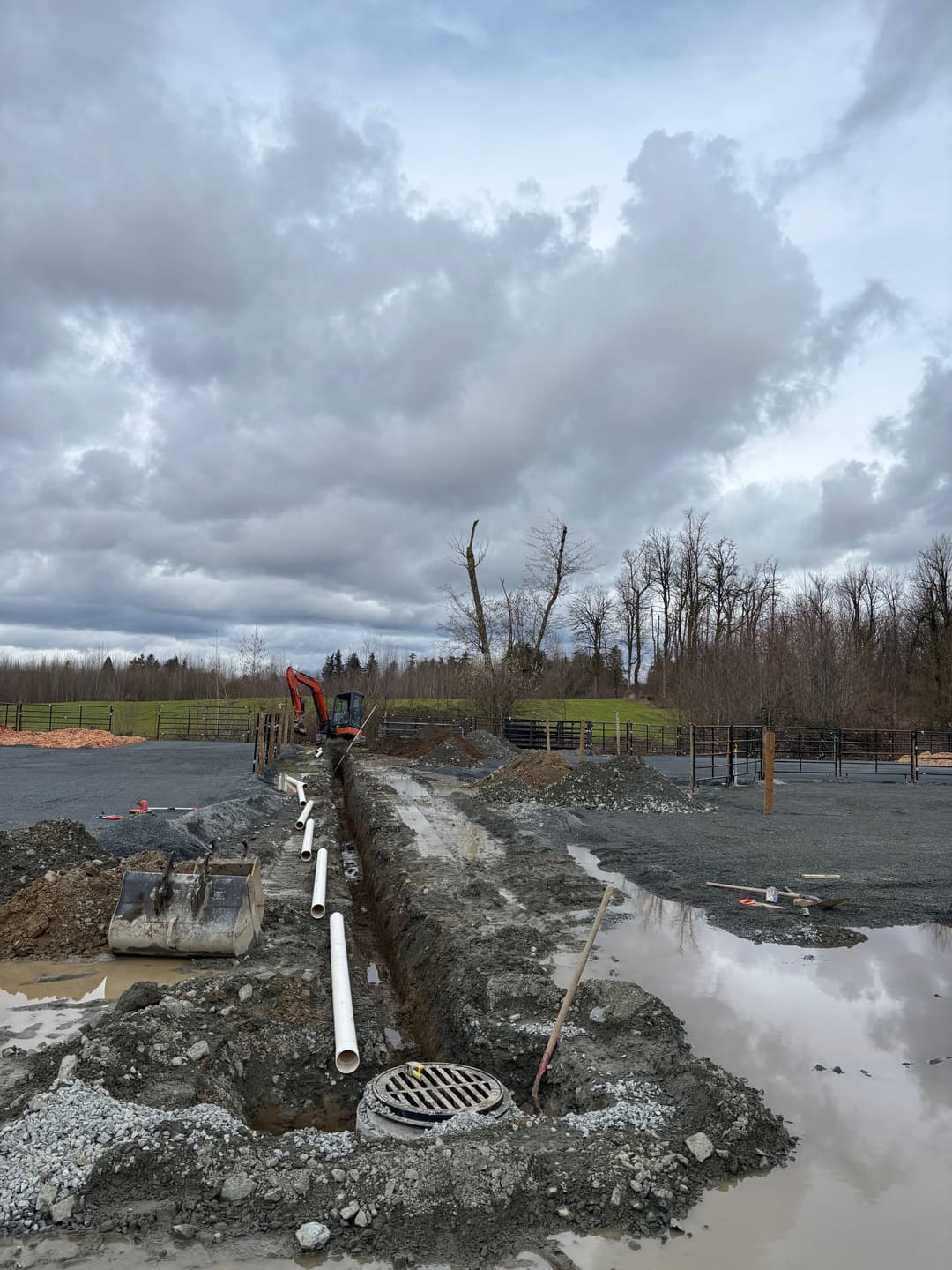 Excavation site with heavy machinery, pipe installation, and cloudy sky in the background.
