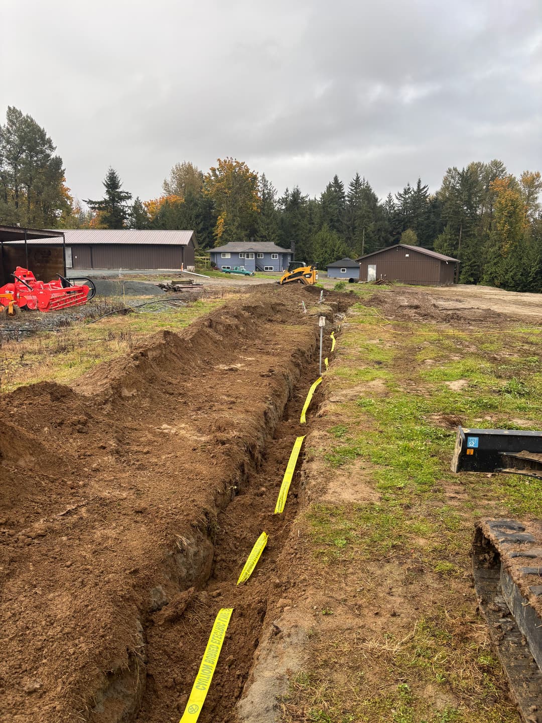 Excavated trench for utility installation with yellow marking tape in rural landscape.