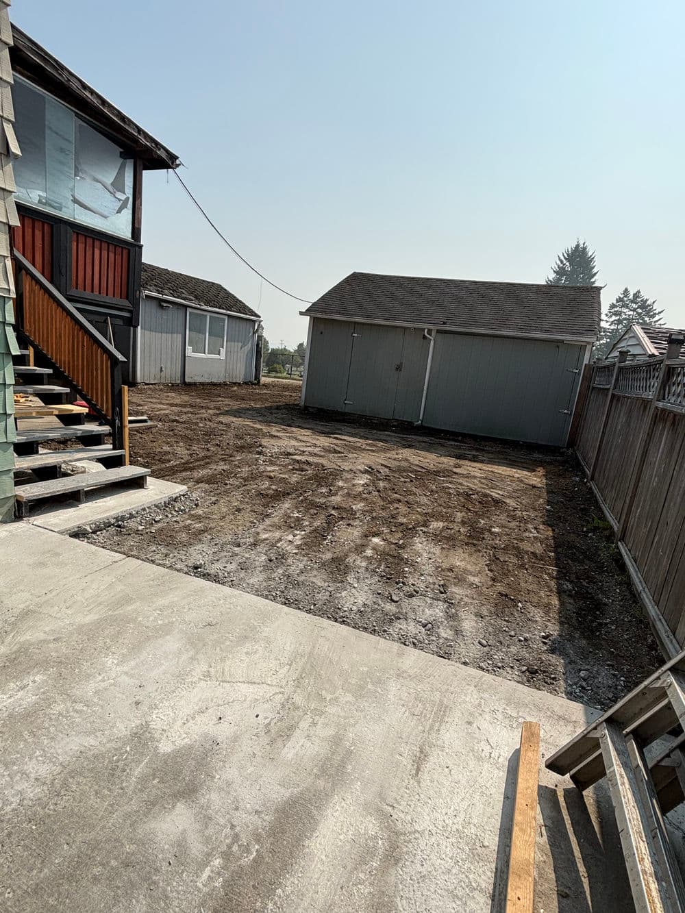 cleared backyard with a shed and stairs leading to a house, under a clear sky