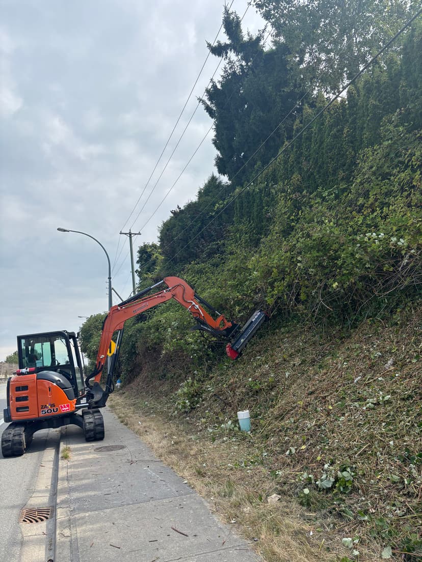 Excavator using an attachment to trim shrubs along a roadside.
