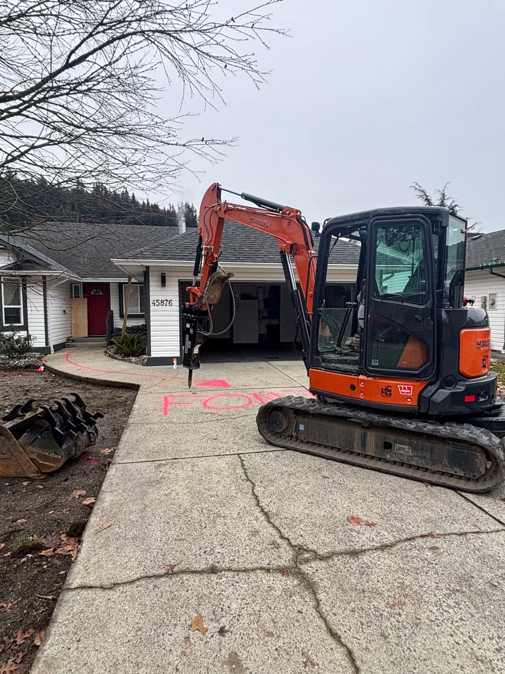 Excavator parked on driveway with marked area for construction near a residential home.