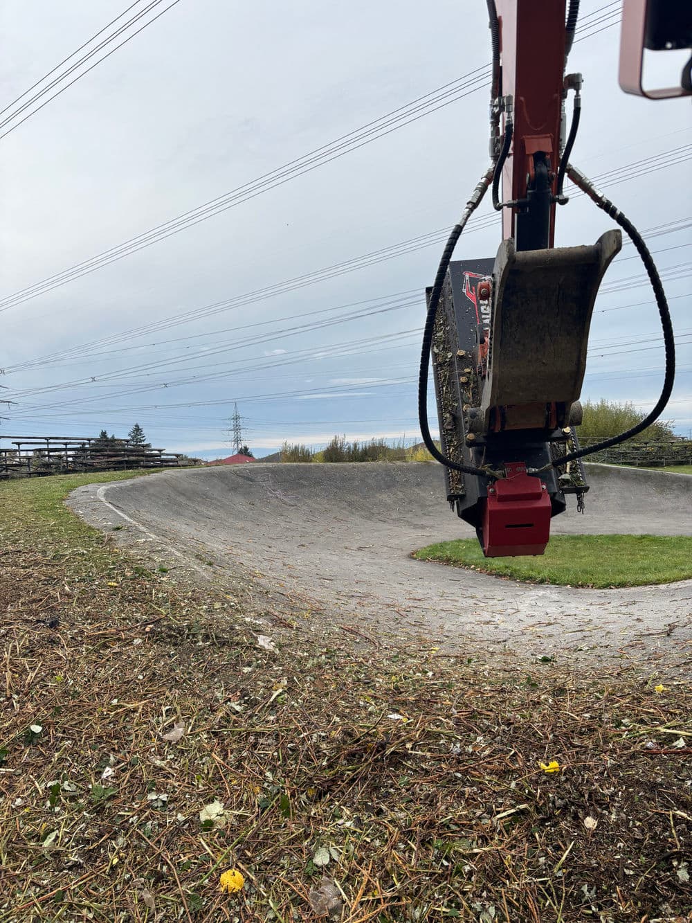 Excavator clearing overgrown vegetation along a curved dirt path under power lines.