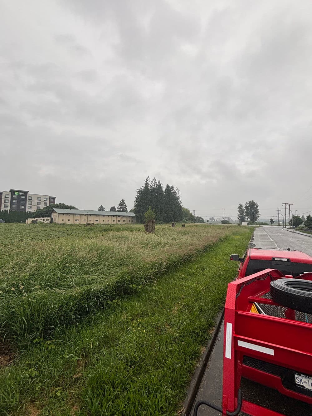 Red farm equipment near a field under a cloudy sky with distant buildings and trees.